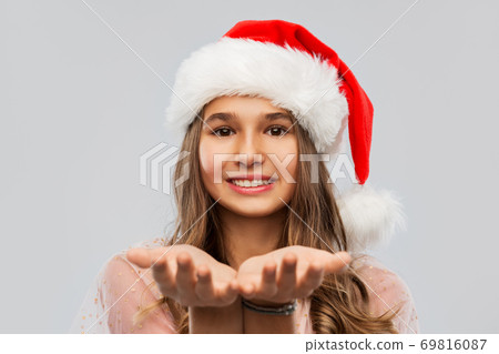happy teenage girl in santa hat holding something 69816087