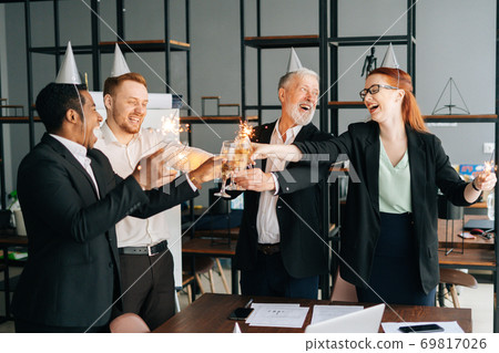Cheerful business team of multiethnic coworkers holding Bengal lights, clinking glasses of champagne 69817026