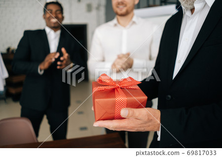 Close-up of hands of unrecognizable mature man holding red gift box tied to bow. 69817033