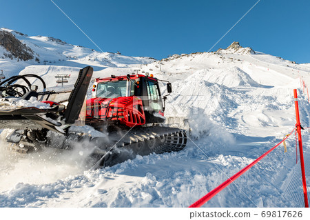 Red modern snowcat ratrack with snowplow snow grooming machine preparing ski slope piste hill at alpine skiing winter resort Ischgl in Austria. Heavy machinery mountain equipment track vehicle 69817626