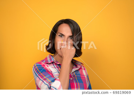 Brunette woman covers her nose with her hand. The unpleasant smell of the concept. Shooting in the studio on a yellow background. High quality photo 69819069