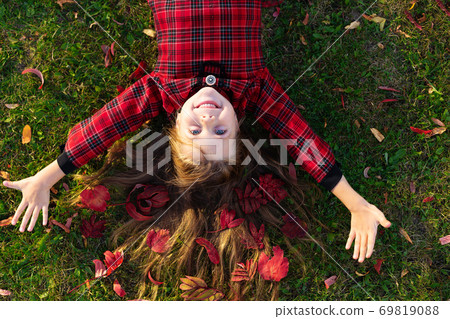 A beautiful girl lies on the ground with autumn leaves in her hair. 69819088