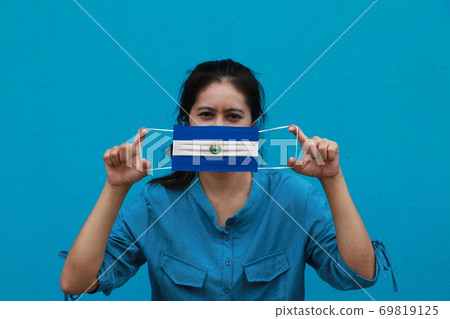 A woman and hygienic mask with El Salvador flag pattern in her hand and raises it to cover her face A woman and hygienic mask with El Salvador flag pattern in her hand and raises it to cover her face 69819125