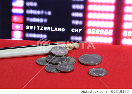 Heap of Swiss coins with white and black pencil on the red floor and digital board Heap of Swiss coins with white and black pencil on the red floor and digital board 69819153