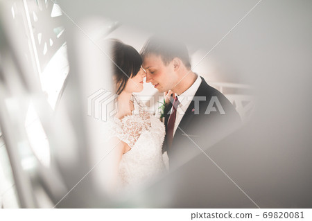 Lovely happy wedding couple, bride with long white dress posing in beautiful city Lovely happy wedding couple, bride with long white dress posing in beautiful city 69820081