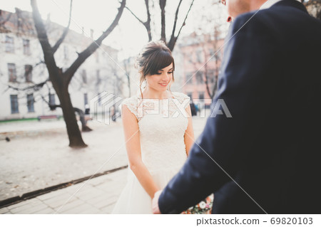 Stylish couple of happy newlyweds walking in the park on their wedding day with bouquet Stylish couple of happy newlyweds walking in the park on their wedding day with bouquet 69820103