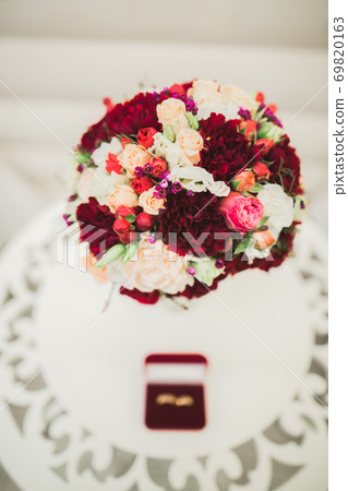 Beautiful toned picture with wedding rings against the background of a bouquet of flowers Beautiful toned picture with wedding rings against the background of a bouquet of flowers 69820163