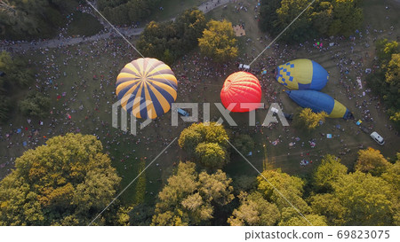 Aerial view of people looking at how hot air balloons prepare for an summer evening flying in park in small european city 69823075