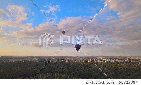 Aerial drone view of colorful hot air balloon flying over green park in small european city at summer sunset Aerial drone view of colorful hot air balloon flying over green park in small european city at summer sunset 69823087