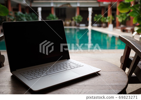 A white laptop on wooden table swiming pool background. 69823271