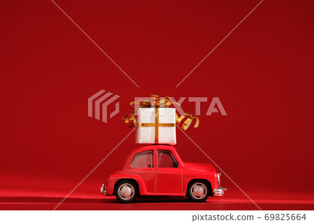 Red small retro toy car with gift on the roof on red background. Delivery. New Year, Christmas, Valentines Day, World Womans Day, Sale concept. Red small retro toy car with gift on the roof on red background. Delivery. New Year, Christmas, Valentines Day, World Womans Day, Sale concept. 69825664