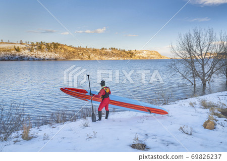 active senior is carrying stand up paddleboard in winter 69826237