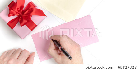 Pink gift box with red bow and male hands writing love letter, greeting card for Valentine's day or wedding invitation. Top view. White background. Pink gift box with red bow and male hands writing love letter, greeting card for Valentine's day or wedding invitation. Top view. White background. 69827328