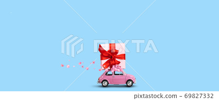 Pink car with gift box on a roof with flowers on a blue background. Pink car with gift box on a roof with flowers on a blue background. 69827332