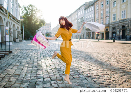 Pretty brown-haired young excited woman, wearing trendy yellow suit, satisfied after successful shopping , and jumping with colourful shopping bags. Shopping in the city Pretty brown-haired young excited woman, wearing trendy yellow suit, satisfied after successful shopping , and jumping with colourful shopping bags. Shopping in the city 69829771
