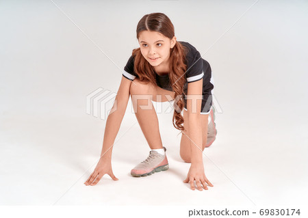 Being active. Full length of cute teenage girl in sportswear standing in start position and smiling isolated over grey background in studio Being active. Full length of cute teenage girl in sportswear standing in start position and smiling isolated over grey background in studio 69830174