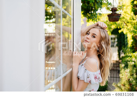 girl in summer dress standing by window in garden girl in summer dress standing by window in garden 69831108