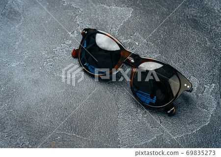 Dark male sunglasses on grey concrete surface Dark male sunglasses on grey concrete surface 69835273