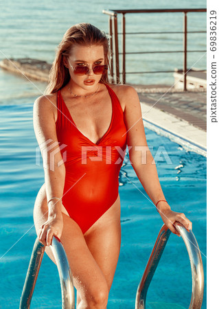 Attractive woman in red swimsuit and sunglasses coming out of the pool 69836219