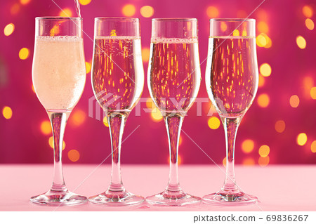 Four champagne glasses against pink background with blurred garland Four champagne glasses against pink background with blurred garland 69836267