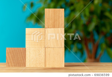 Wooden blocks on desk against blurred plant background Wooden blocks on desk against blurred plant background 69836599