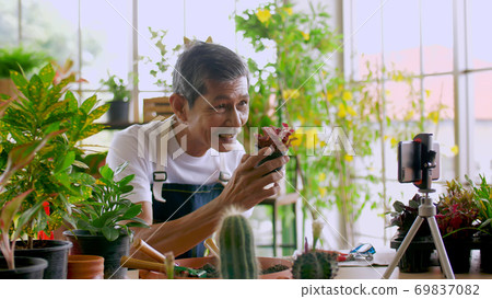 Senior gardener man selling beautiful plants on social media by streaming live from his shop. 69837082