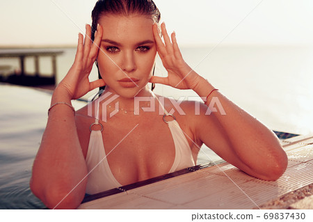 Portrait of a woman in white bikini sitting in a pool 69837430