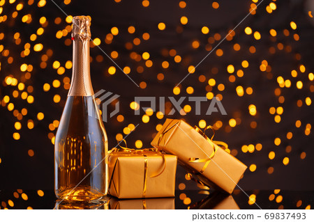 Champagne bottle and wrapped gift on blurred background of Christmas lights 69837493
