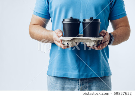 Man coffee shop worker giving takeaway cups of coffee on grey background Man coffee shop worker giving takeaway cups of coffee on grey background 69837632