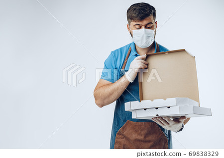 Pizza delivery man in medical gloves and mask. Safe service while coronavirus covid-19 outbreak Pizza delivery man in medical gloves and mask. Safe service while coronavirus covid-19 outbreak 69838329