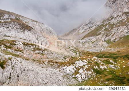 rocky alpine gorge partially obscured by a cloud 69845281