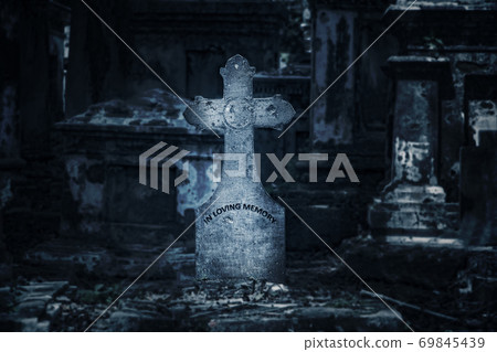 The ancient tombstone with cross at night with moonlight, on background the cemetery. 69845439