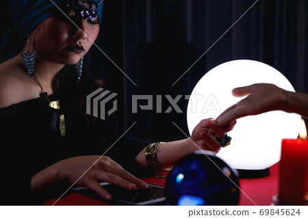 Fortune teller reading customer's palm to forecast future or fate by using digital tablet. Fortune teller reading customer's palm to forecast future or fate by using digital tablet. 69845624