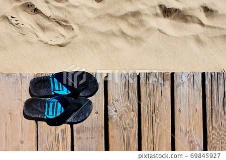 Men's slippers and Wooden walkway on the sandy beach. Wooden boardwalk and light soft sand. Top view. 69845927
