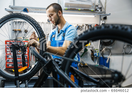 Bicycle repair in workshop, man setting up brake 69846012