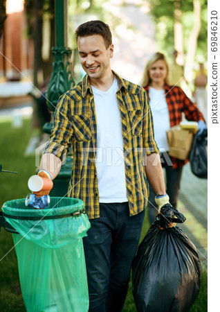 Young man puts garbage in plastic bag in park Young man puts garbage in plastic bag in park 69846210
