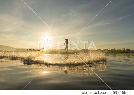 Silhouette Fisherman casting or throwing a net for catching freshwater fish in nature lake or river with reflection in morning time in Asia in Thailand. People. 69846664