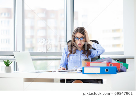 Young office worker sitting at desk holding head because of pain in office Young office worker sitting at desk holding head because of pain in office 69847901
