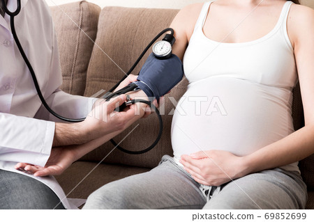 Young doctor is checking blood pressure of pregnant woman at home. High pressure problem during pregnancy concept Young doctor is checking blood pressure of pregnant woman at home. High pressure problem during pregnancy concept 69852699