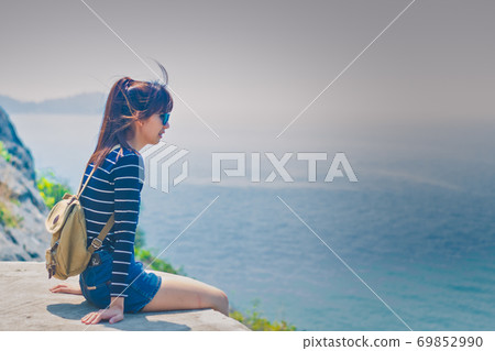 Happy traveler Asian woman sitting on a cliff that sees the sea beach at Ko Sichang, Thailand. Summer travel vacation concept. Happy traveler Asian woman sitting on a cliff that sees the sea beach at Ko Sichang, Thailand. Summer travel vacation concept. 69852990