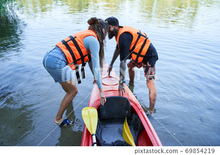 Man and woman in safe jackets pulling canoe Man and woman in safe jackets pulling canoe 69854219