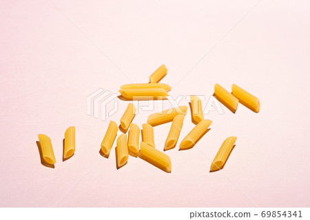 Italian pasta, raw penne tube macaroni on bright pink pastel background, angle view, abstract food 69854341