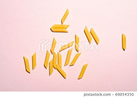 Italian pasta, raw penne tube scattered macaroni on bright pink cream background, top view copy space, abstract food 69854350