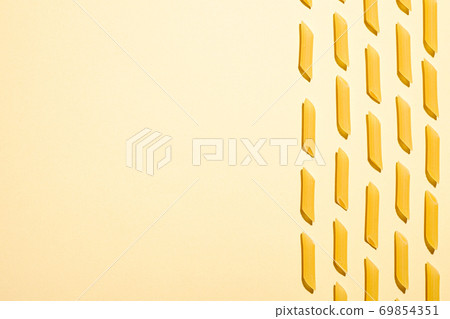 Italian pasta, raw penne tube macaroni pattern on yellow cream background, top view copy space, abstract food 69854351