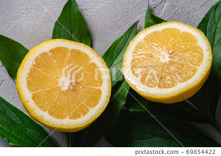 Two lemon slices, tropical citrus fruits with green leaves on grey concrete background, top view macro Two lemon slices, tropical citrus fruits with green leaves on grey concrete background, top view macro 69854422