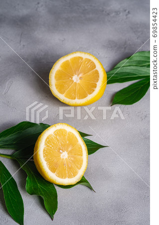 Two lemon slices, tropical citrus fruits with green leaves on grey concrete background, angle view Two lemon slices, tropical citrus fruits with green leaves on grey concrete background, angle view 69854423