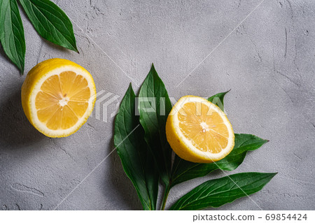 Two lemon slices, tropical citrus fruits with green leaves on grey concrete background, top view Two lemon slices, tropical citrus fruits with green leaves on grey concrete background, top view 69854424