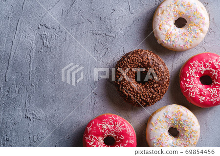 Chocolate, pink and vanilla donuts with sprinkles, sweet glazed dessert food on concrete textured background, top view copy space 69854456