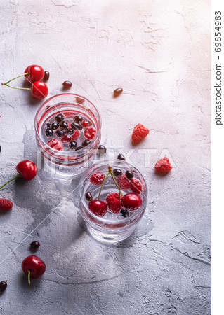 Fresh cold sparkling water drink with cherry, raspberry and currant berries in two transparent glass on stone concrete background, summer diet beverage, angle view 69854983