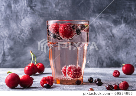 Fresh cold sparkling water drink with cherry, raspberry and currant berries in red faceted glass on stone concrete background, summer diet beverage, angle view 69854995